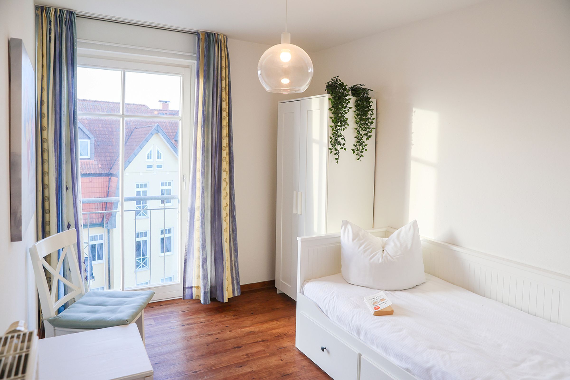 A bedroom with a bed, a desk, and a window with curtains.