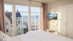 Habitación de hotel con una cama grande, televisión instalada en la pared y vista a la playa y edificios.