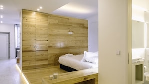 A modern bedroom with a wooden wardrobe, a bed with white linens, and a bedside table with two candles.