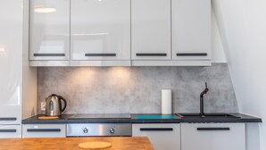 A modern kitchen with white cabinets, a stainless steel kettle, a sink, and a countertop. - Victus Apartamenty - Prestige (Sopot)
