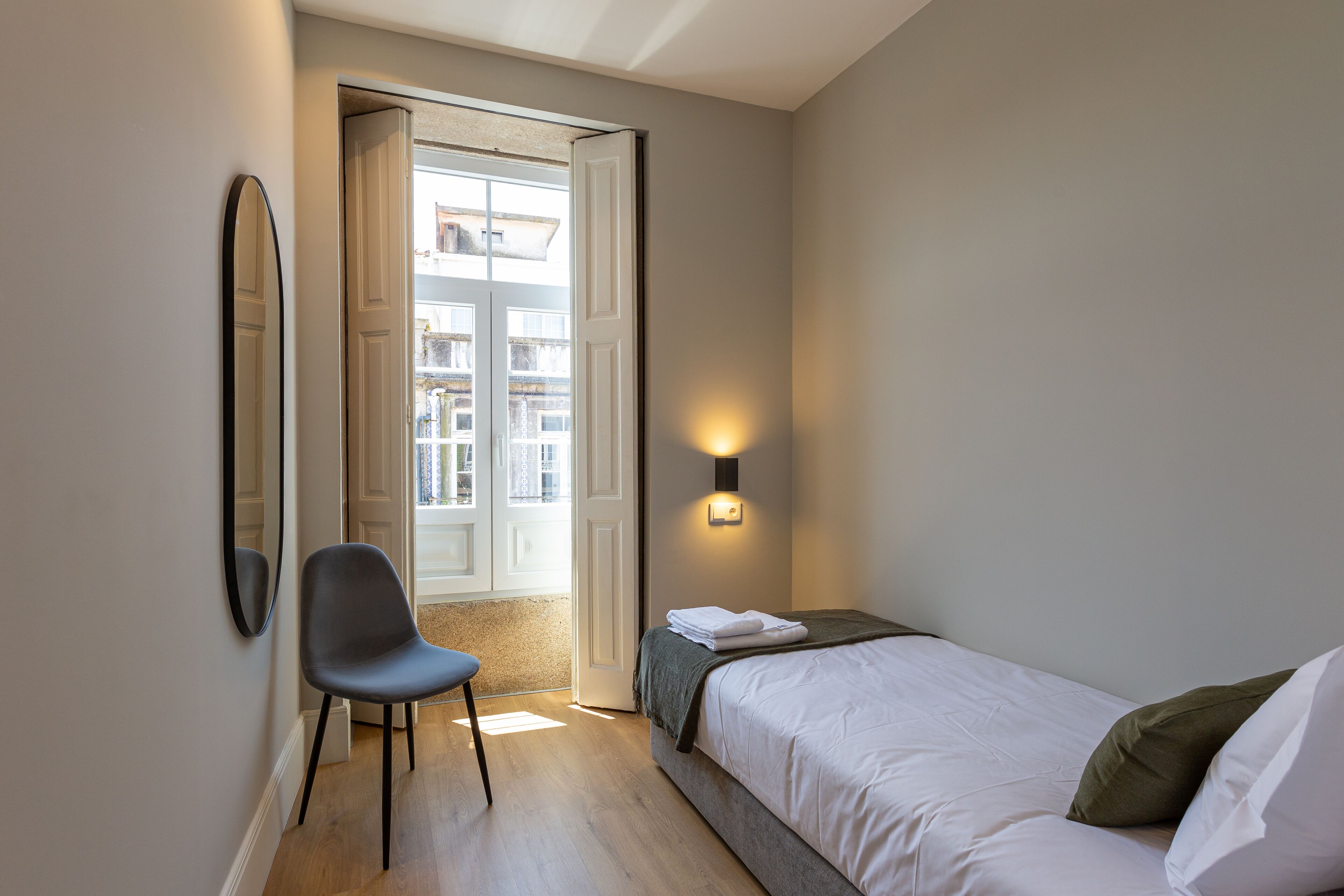 Un dormitorio con cama, una silla, un espejo en la pared y una puerta que da a un balcón.