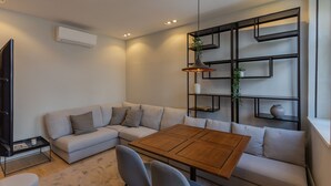 A modern living room with a sectional sofa, a wooden coffee table, and a black shelving unit with plants. - ORM - Bolhao Apartments (Porto)
