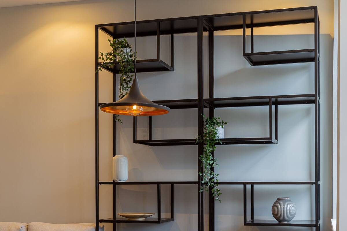A modern living room with a wooden dining table, grey upholstered sofa, and black metal shelving unit.