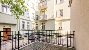 A wooden deck with a metal railing, a parked car, and a building with multiple windows and balconies. - Victus Apartamenty - Anda (Sopot)