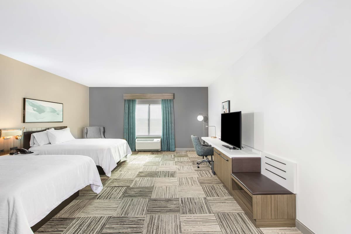 Ein Hotelzimmer mit zwei Betten, einem Schreibtisch, einem Fernseher und einem Fenster mit Vorhängen.