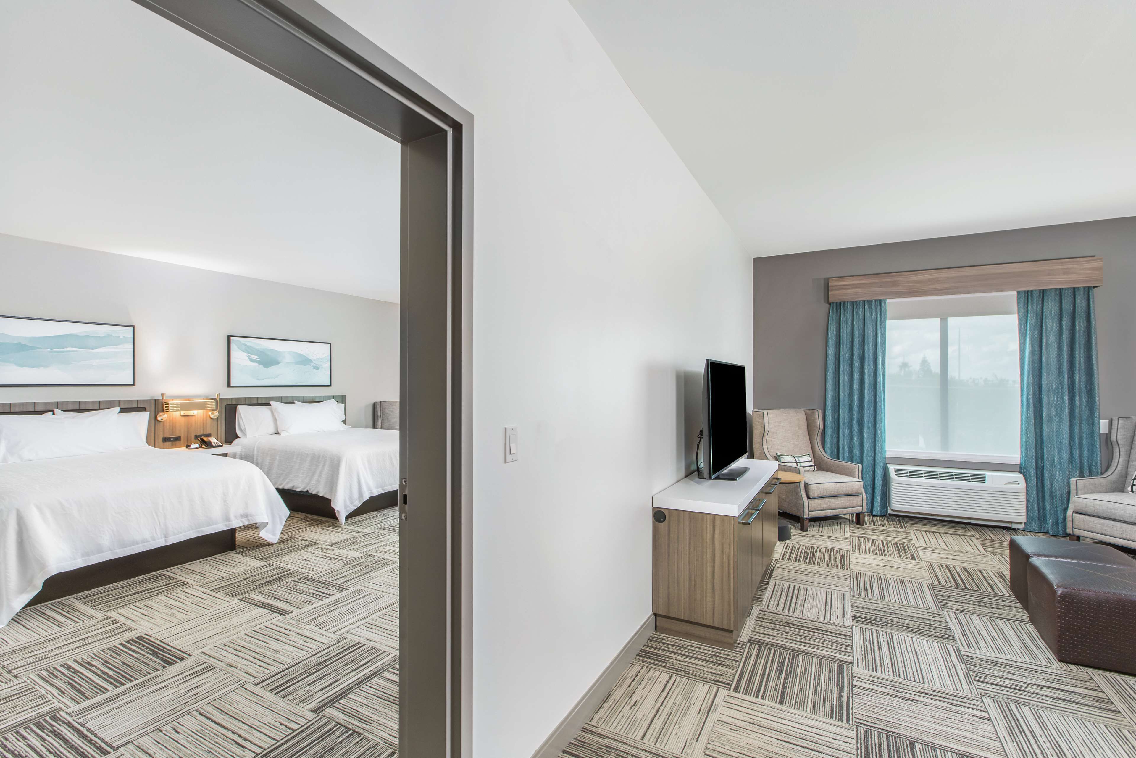A hotel room with two beds, a TV, a desk, a chair, and a large window with curtains.