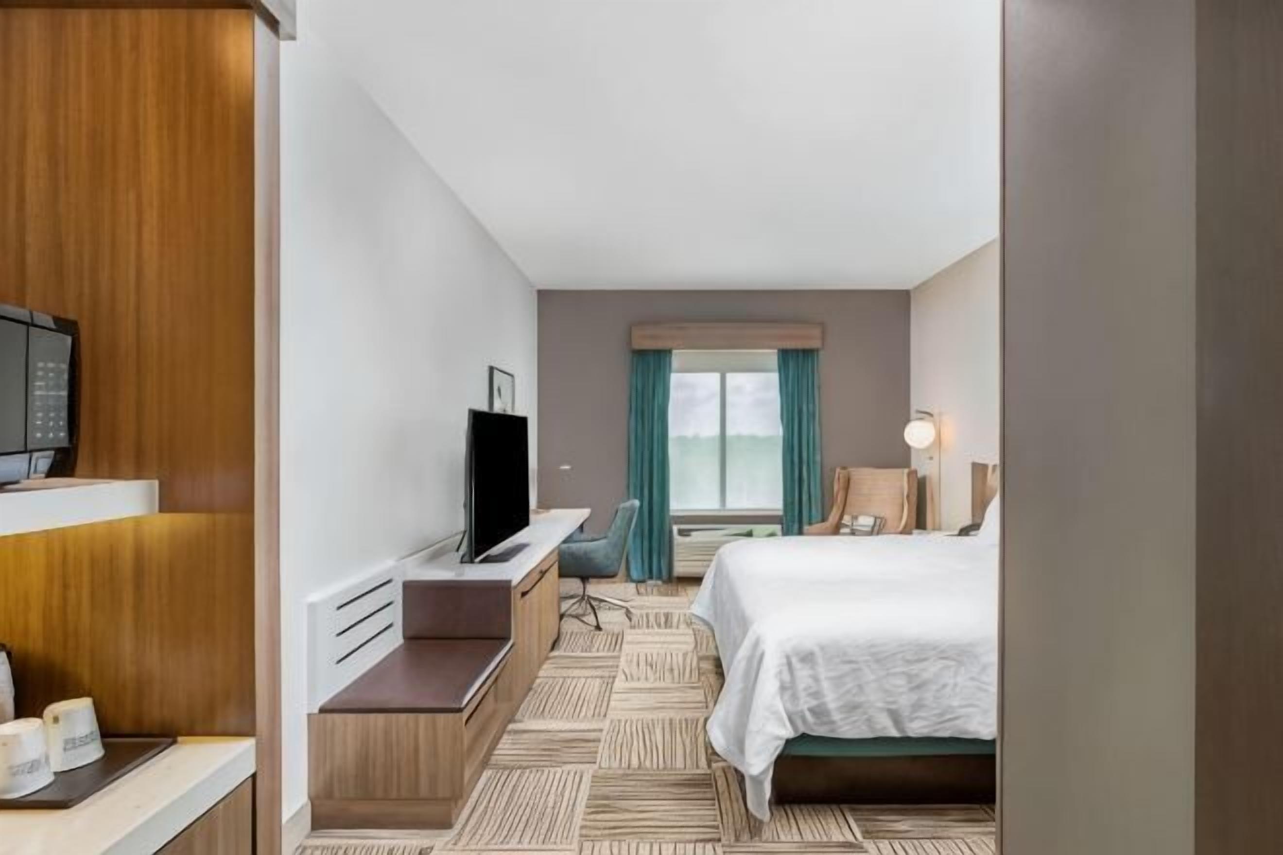 A hotel room with a bed, a desk, a television, and a window with curtains.