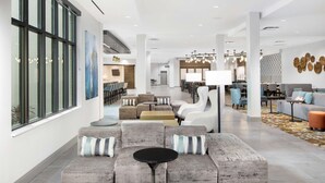 Un hall d’entrée spacieux au design moderne, comprenant un grand espace salon avec des canapés et des fauteuils, une table basse et, au fond, un coin repas.