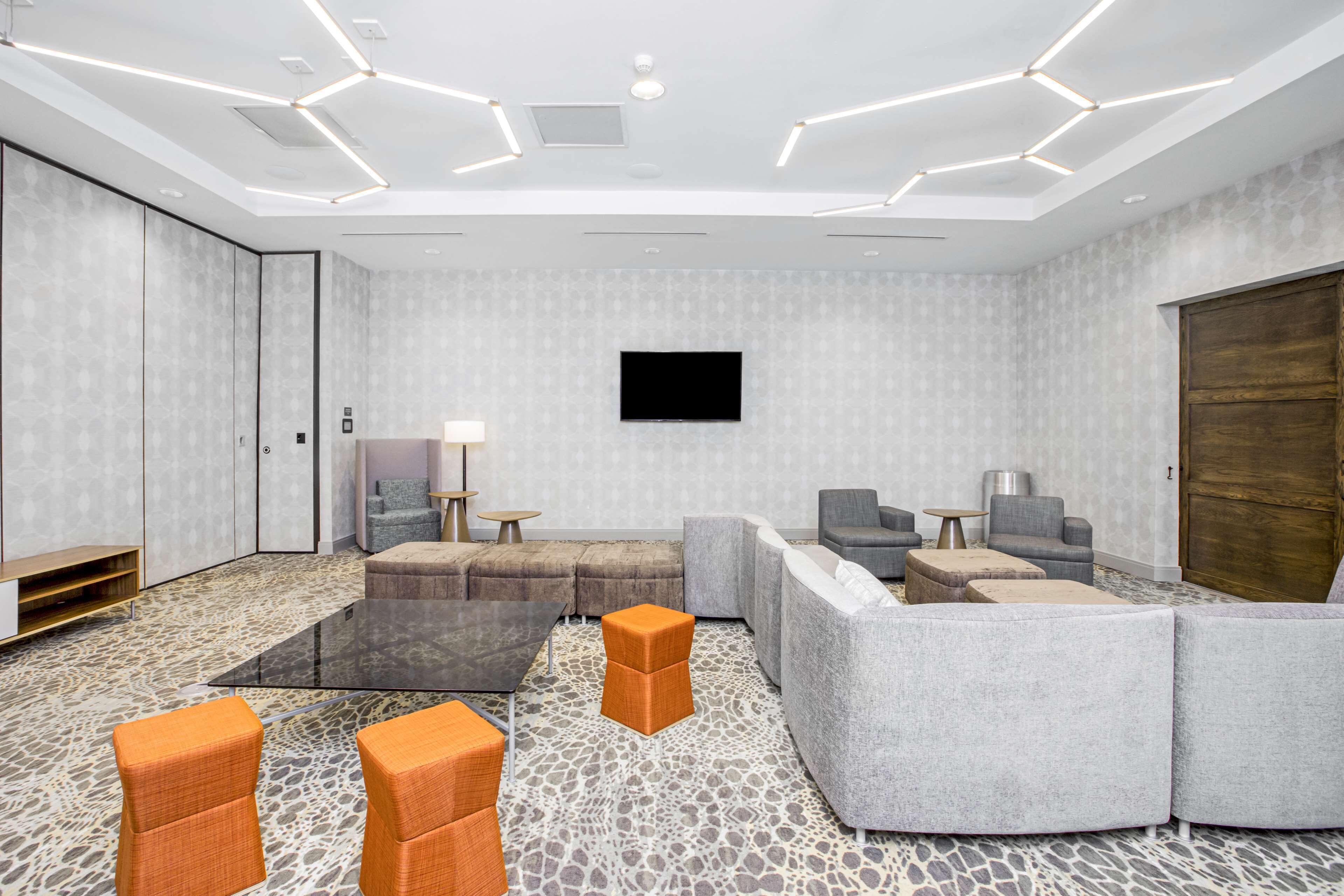 A modern lounge area with a large sectional sofa, a glass coffee table, and orange accent chairs.