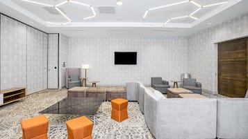 A modern lounge area with a large sectional sofa, a glass coffee table, and orange accent chairs.