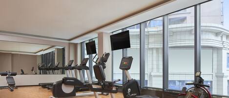 Un gimnasio moderno con máquinas de cardio, bancos de pesas y un espejo grande.