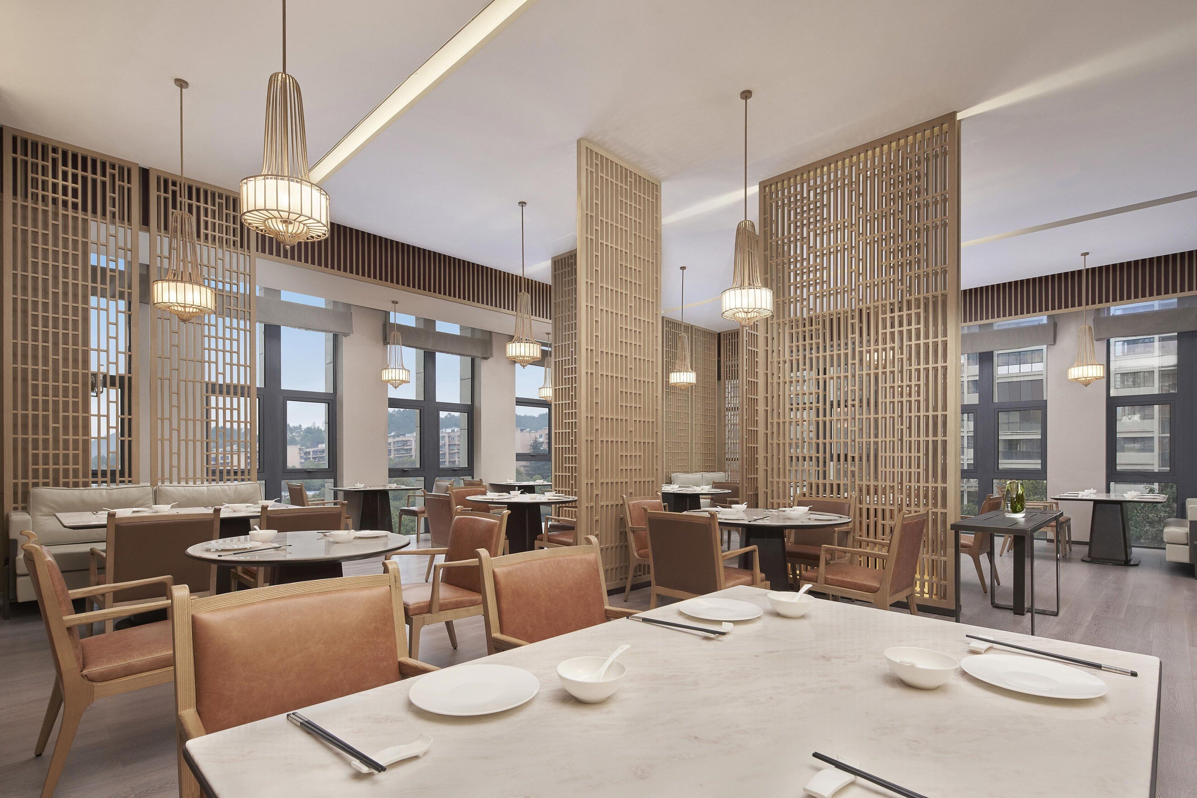 Un restaurante moderno con techos altos, luz natural y una combinación de mesas redondas y rectangulares.