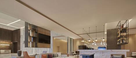A modern hotel lobby with a seating area, a reception desk, and a kitchen in the background.