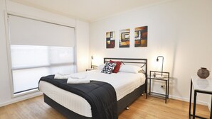 Ein Schlafzimmer mit Bett, Nachttischen, einem Fenster mit Jalousien und Wandbildern.