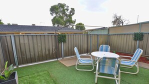 Ein Garten mit Kunstrasen, einem Metalltisch und gestreiften Stühlen.
