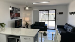 Eine moderne Küche mit Mikrowelle, einer Kochinsel mit Glasplatte und einem Essbereich mit schwarzem Sofa und Glastisch.