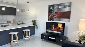 Eine moderne Küche mit weißer Arbeitsplatte, zwei Barhocker und einem schwarzen Sofa.
