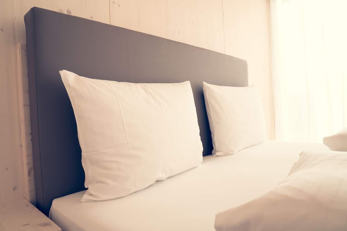 A bed with white bedding and a dark headboard in a room with wooden walls.