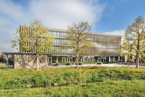 Een modern gebouw met een glazen gevel en een aangelegde binnentuin met bomen en gras.