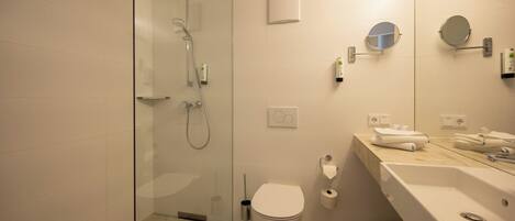 Un baño moderno con ducha de vidrio, inodoro y lavamanos con espejo.