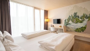 Ein Hotelzimmer mit zwei Betten, einem Schreibtisch, einem Sessel, einem Fernseher und einem Bild an der Wand.