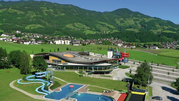 Un hotel moderno con piscina, parco acquatico e vista sulle colline verdi circostanti.