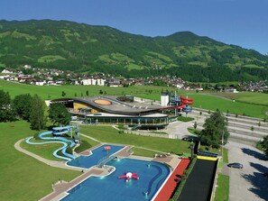 A modern hotel with a swimming pool, a water park, and a view of the surrounding green hills. - Apartment Stumm Near Zillertal Ski Slopes (Stumm)