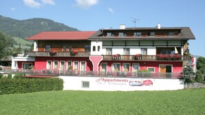 Un edificio a più piani con balconi, un tetto rosso e un cartello pubblicitario che offre appartamenti per 2-10 persone.