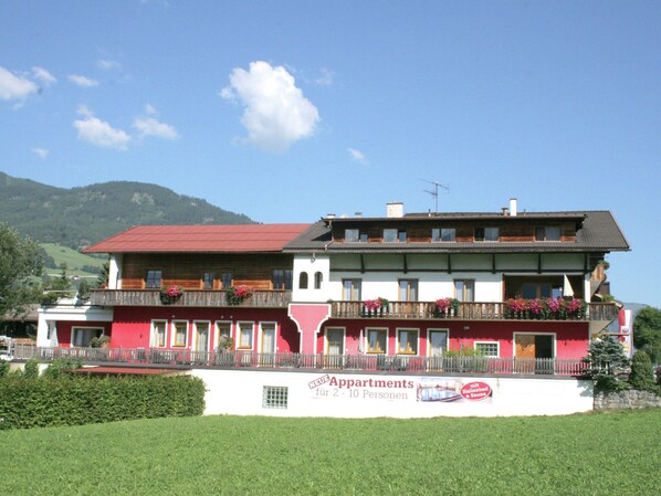 A multi-story building with balconies, a red roof, and a sign advertising apartments for 2-10 people.