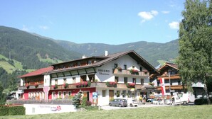 Un edificio in stile alpino tradizionale, con numerosi balconi, un cartello con su scritto "Kaserei Stumm" e vista sulle montagne circostanti.
