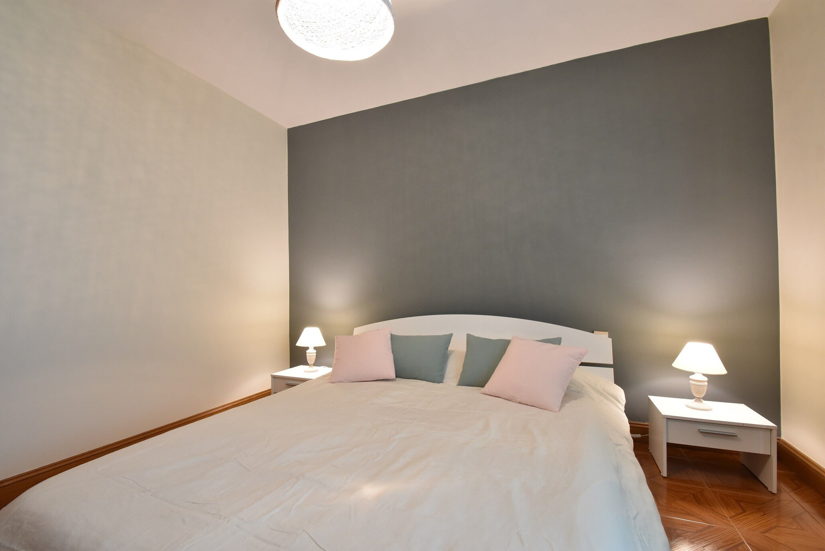 Un dormitorio con una cama, dos mesitas de noche y un aparador con lámparas.
