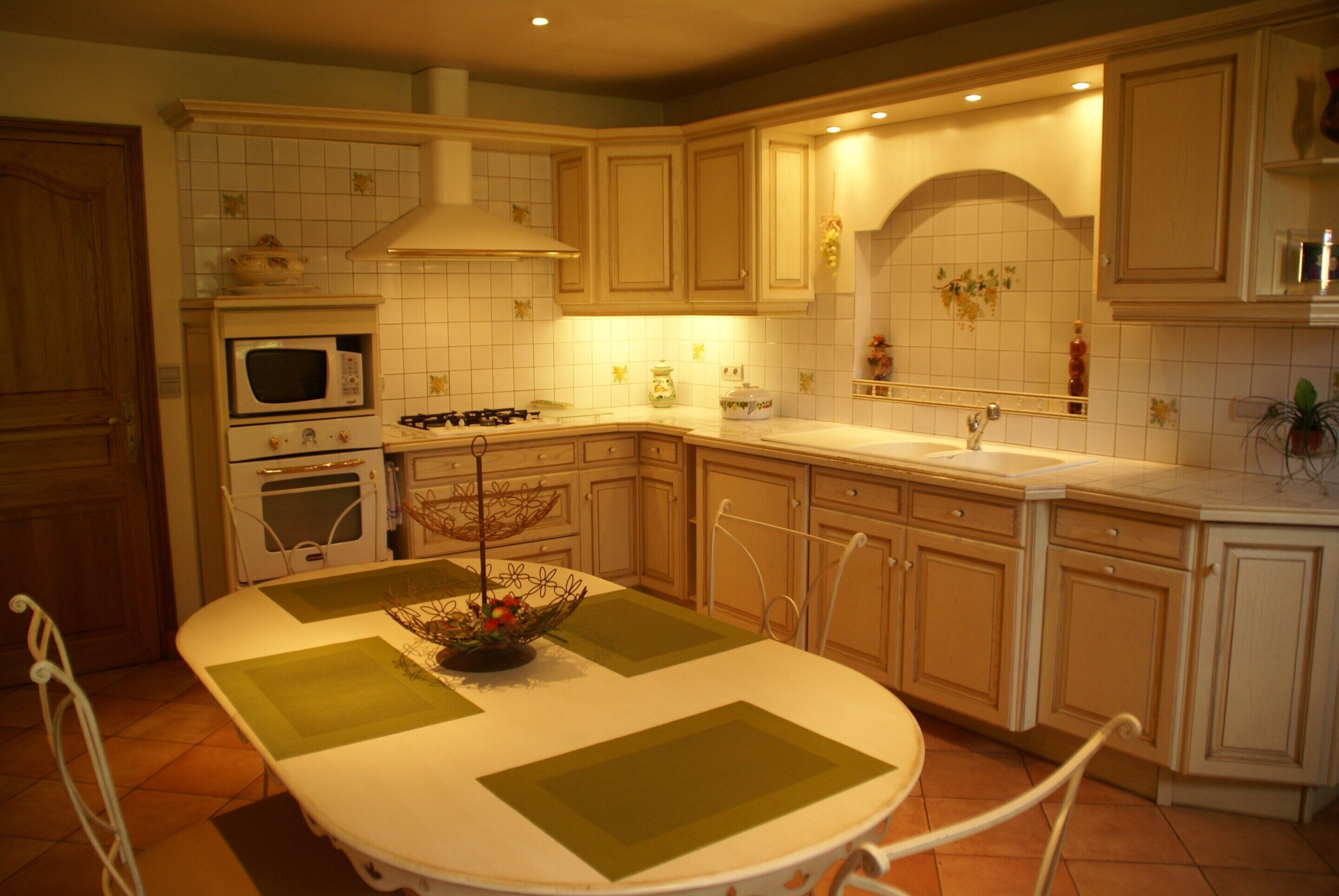 A kitchen with white cabinets, a stove, an oven, a microwave, a dining table with green placemats, and a sink.