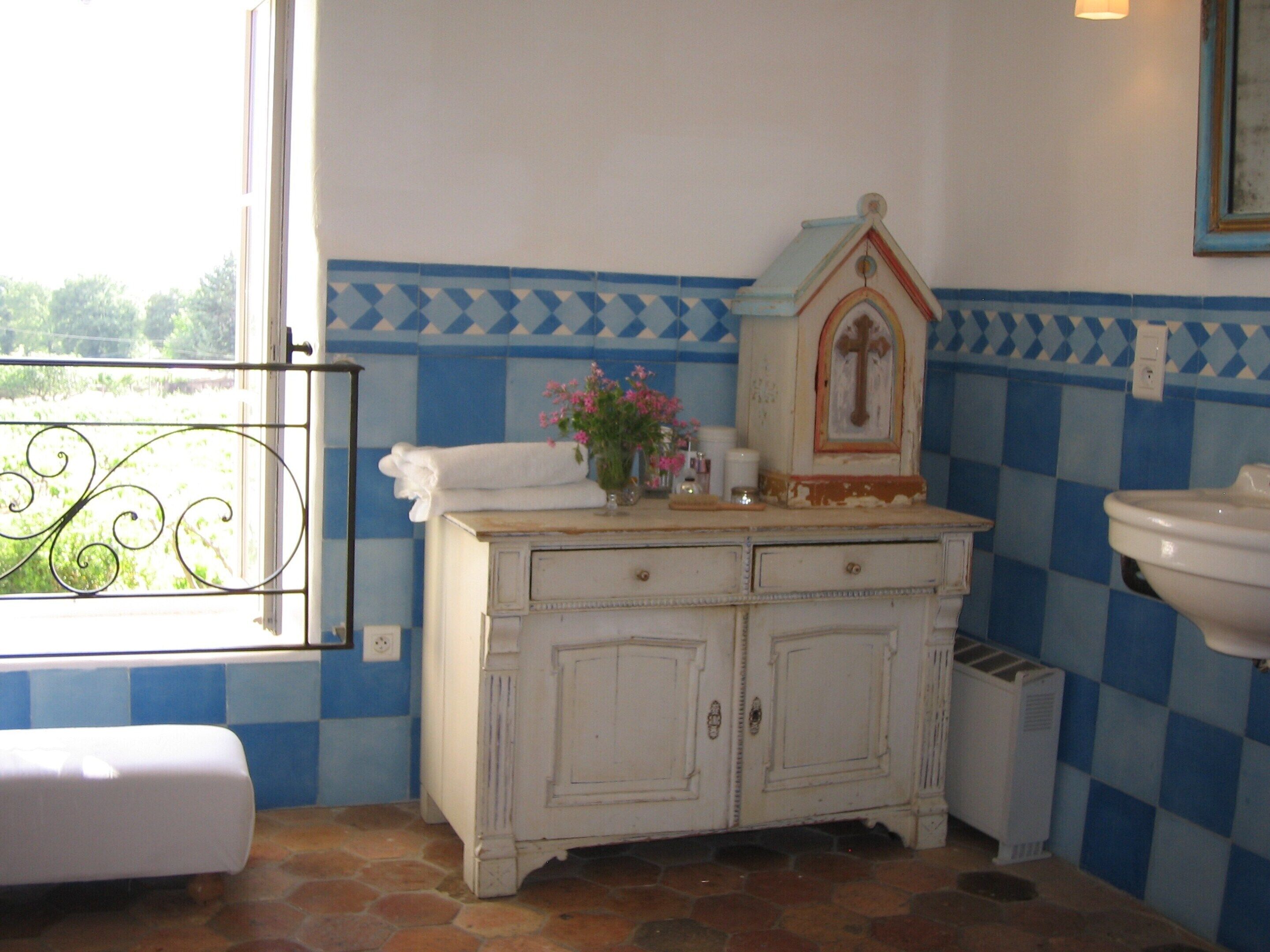 A bathroom with a tiled floor, a white cabinet with two drawers, a white sink, and a window with a view of greenery.