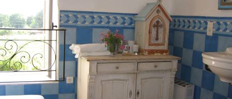 A bathroom with a tiled floor, a white cabinet with two drawers, a white sink, and a window with a view of greenery.