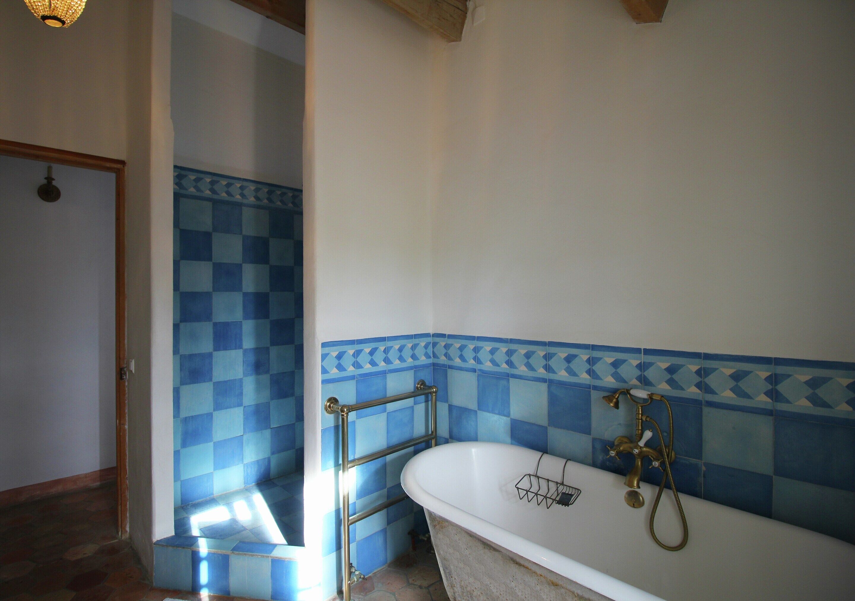 A bathroom with a checkered blue and white tile wall, a white bathtub with a shower head, and a metal towel rack.