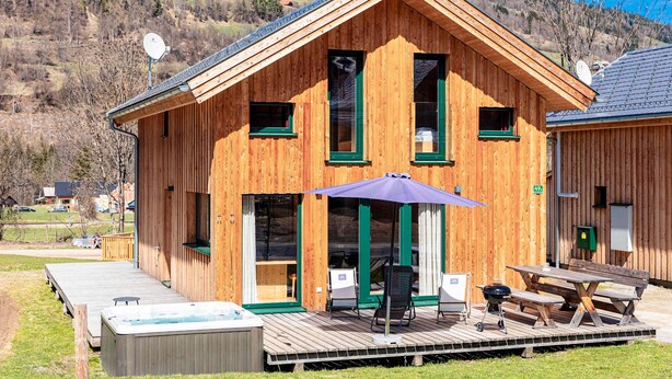 Una cabaña de madera con terraza, asientos exteriores y un jacuzzi.