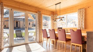 Un interior de madera con zona de comedor, ventanas amplias y vistas a cabañas exteriores.