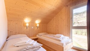 Una habitación de cabaña de madera con dos camas, un ventanal con vistas a un paisaje montañoso y dos lámparas fijadas a la pared.