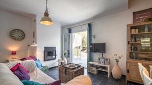 A living room with a sofa, a television, a fireplace, and a large window. - Villa in Pouzols With Private Pool (Pouzols-Minervois)