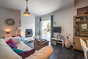 A living room with a sofa, a television, a fireplace, and a large window. - Villa in Pouzols With Private Pool (Pouzols-Minervois)
