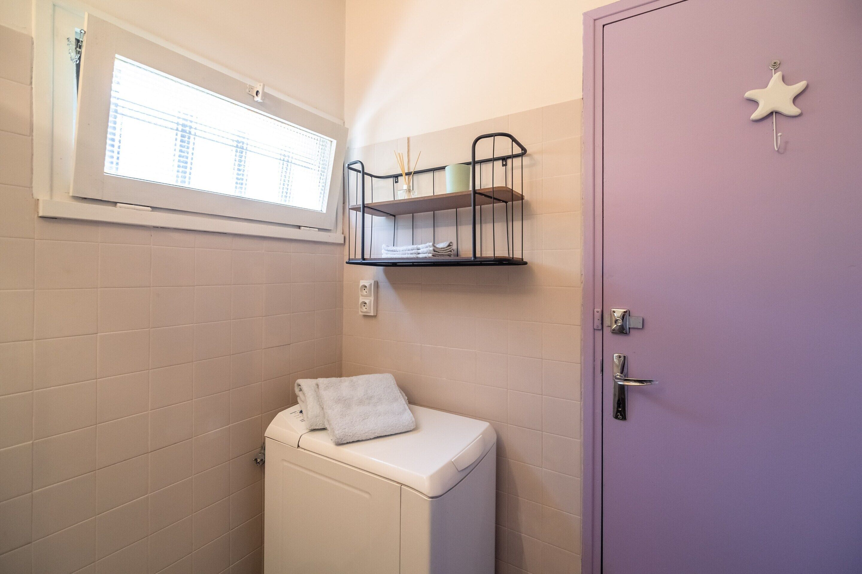 A bathroom with a toilet, a window, a shelf with toiletries, and a door with a star decoration.