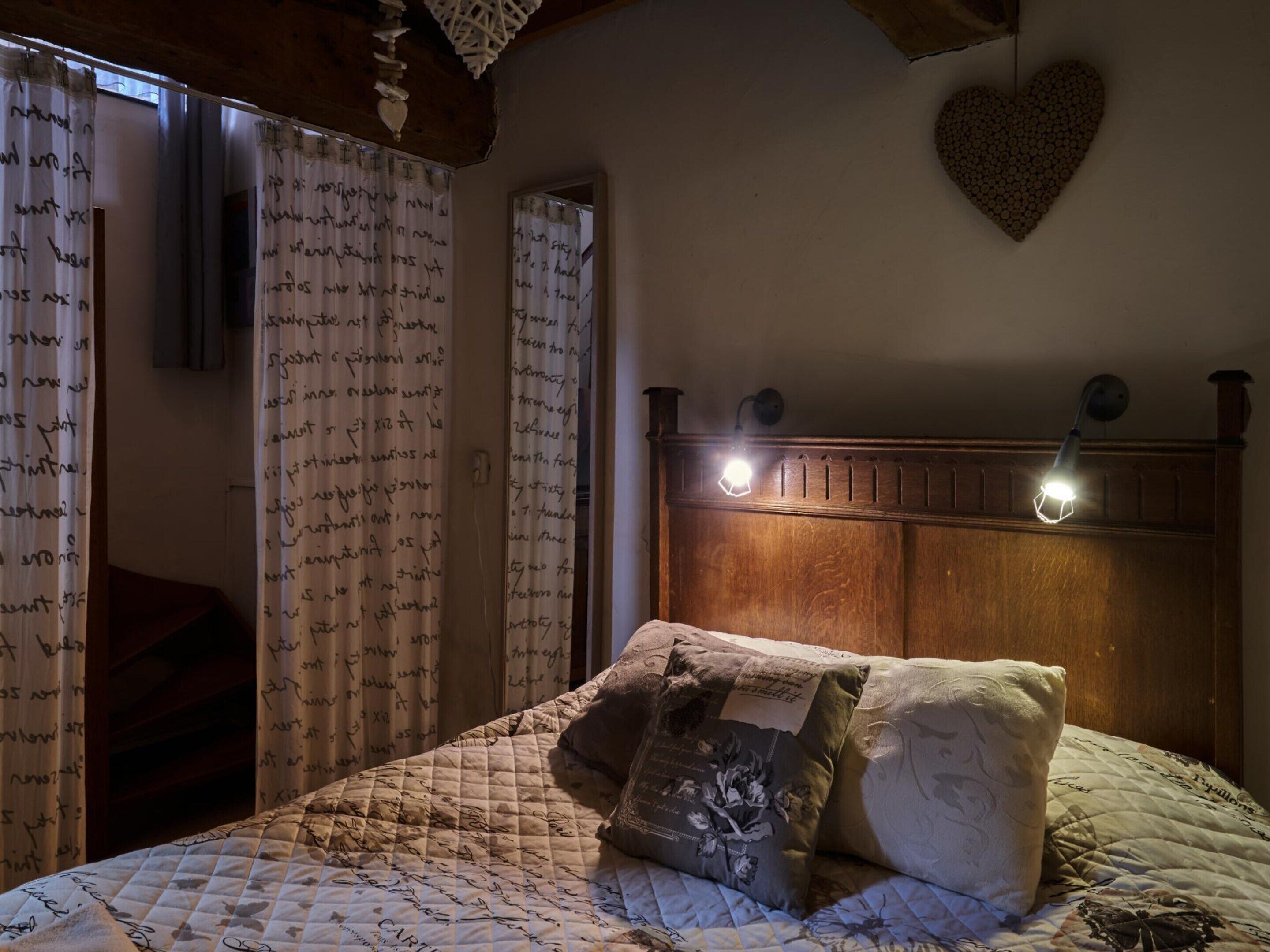Ein Schlafzimmer mit einem hölzernen Kopfteil, einer gesteppten Bettdecke und einer Wanddekoration in Herzform.