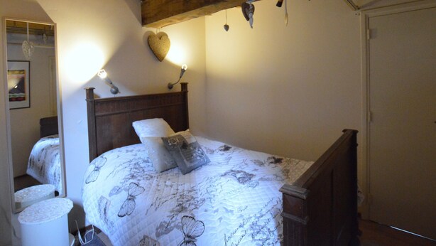 Ein Schlafzimmer mit Holzkopfstütze, einem Bett mit blumigem Überwurf, einer Nachttischlampe und einer herzförmigen Dekoration an der Wand.