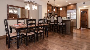 A dining area with a wooden table and chairs, a chandelier, and a kitchen with wooden cabinets and stainless steel appliances.