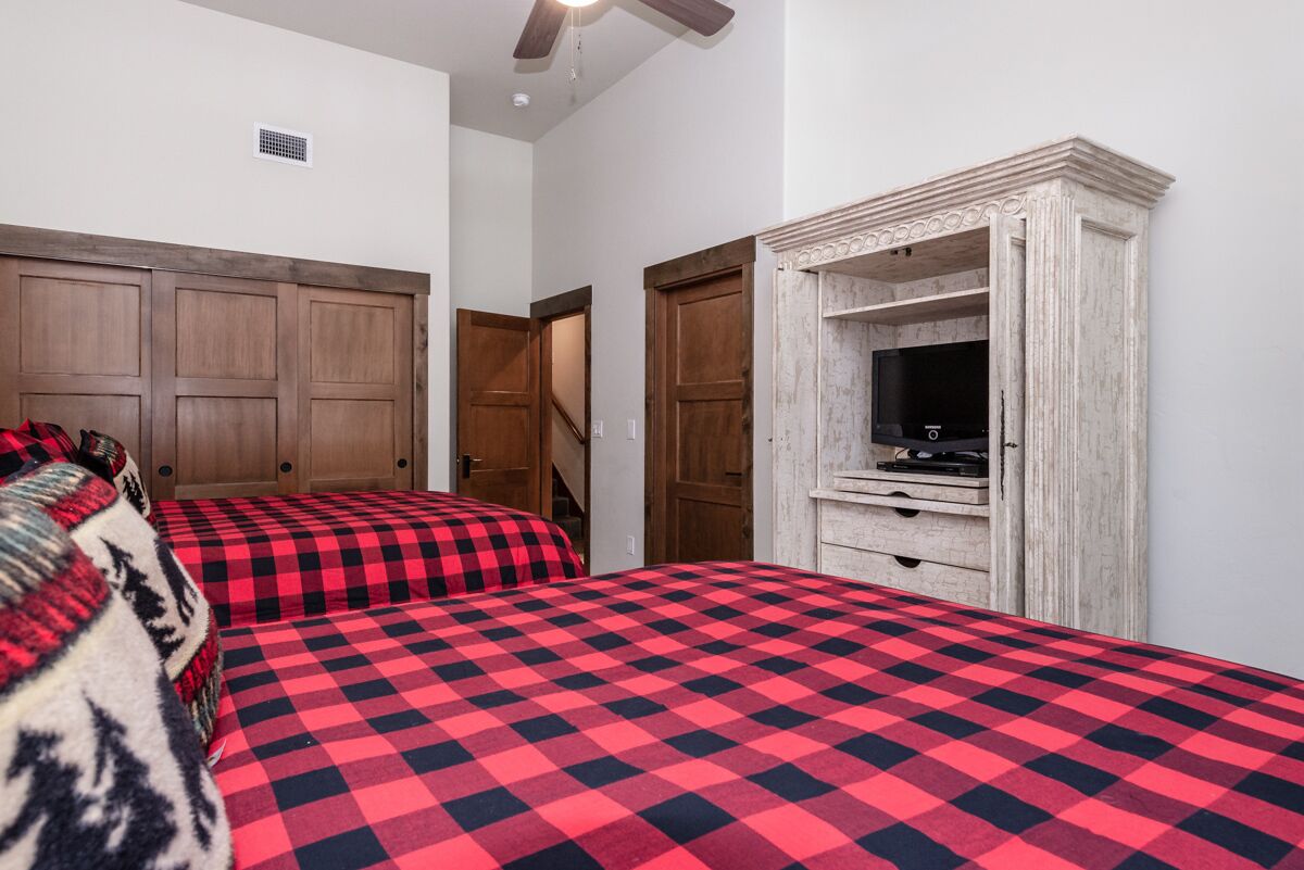 A bedroom with two beds, a wooden wardrobe, and a television on a wooden cabinet.