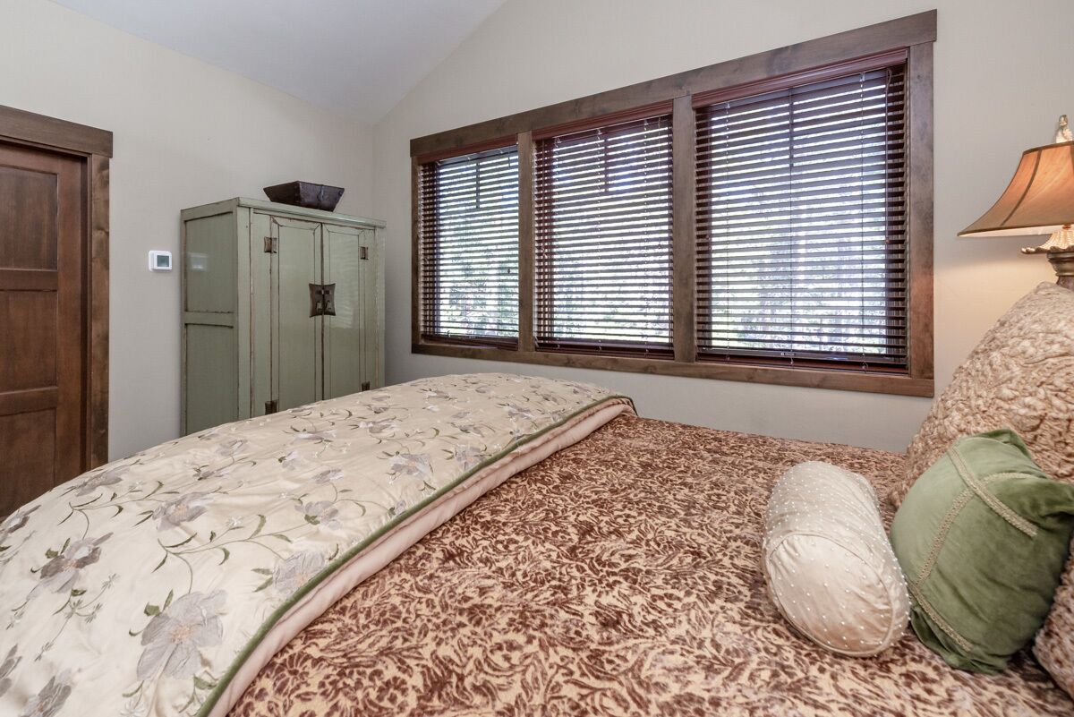 Une chambre à coucher avec un lit, une fenêtre avec des stores, une armoire et une lampe.
