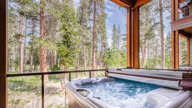 A hot tub with a wooden deck and a view of a forest.