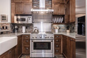 Fully equipped kitchen with stainless steel range hood, microwave, double oven, wooden cabinets, and granite countertop.
