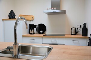 A modern kitchen with a stainless steel sink, wooden countertop, and white cabinetry.