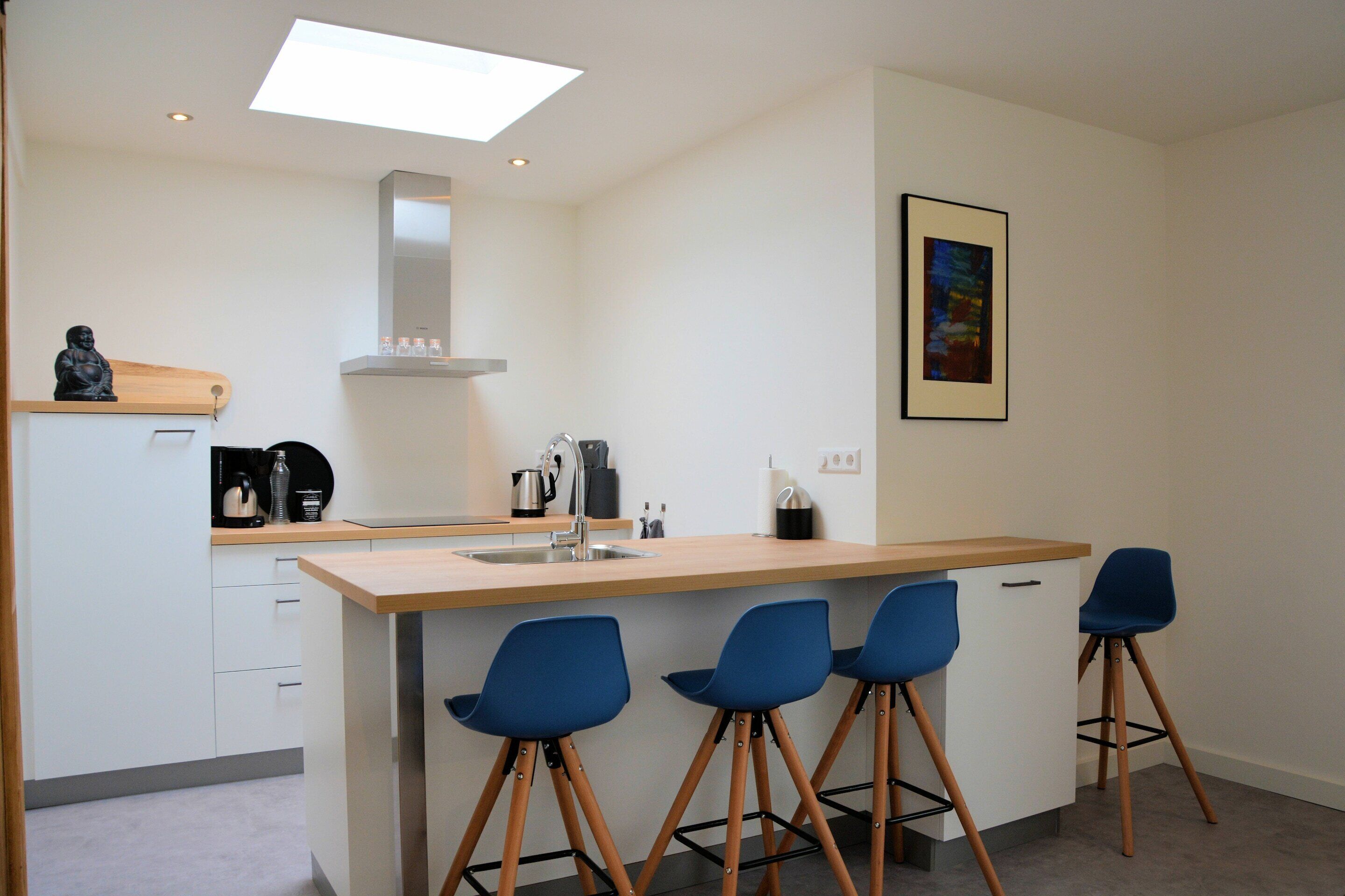 A modern kitchen with a central island, bar stools, and a coffee machine.